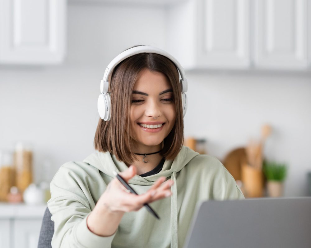 Positive freelancer in headphones having video call on blurred laptop at home
